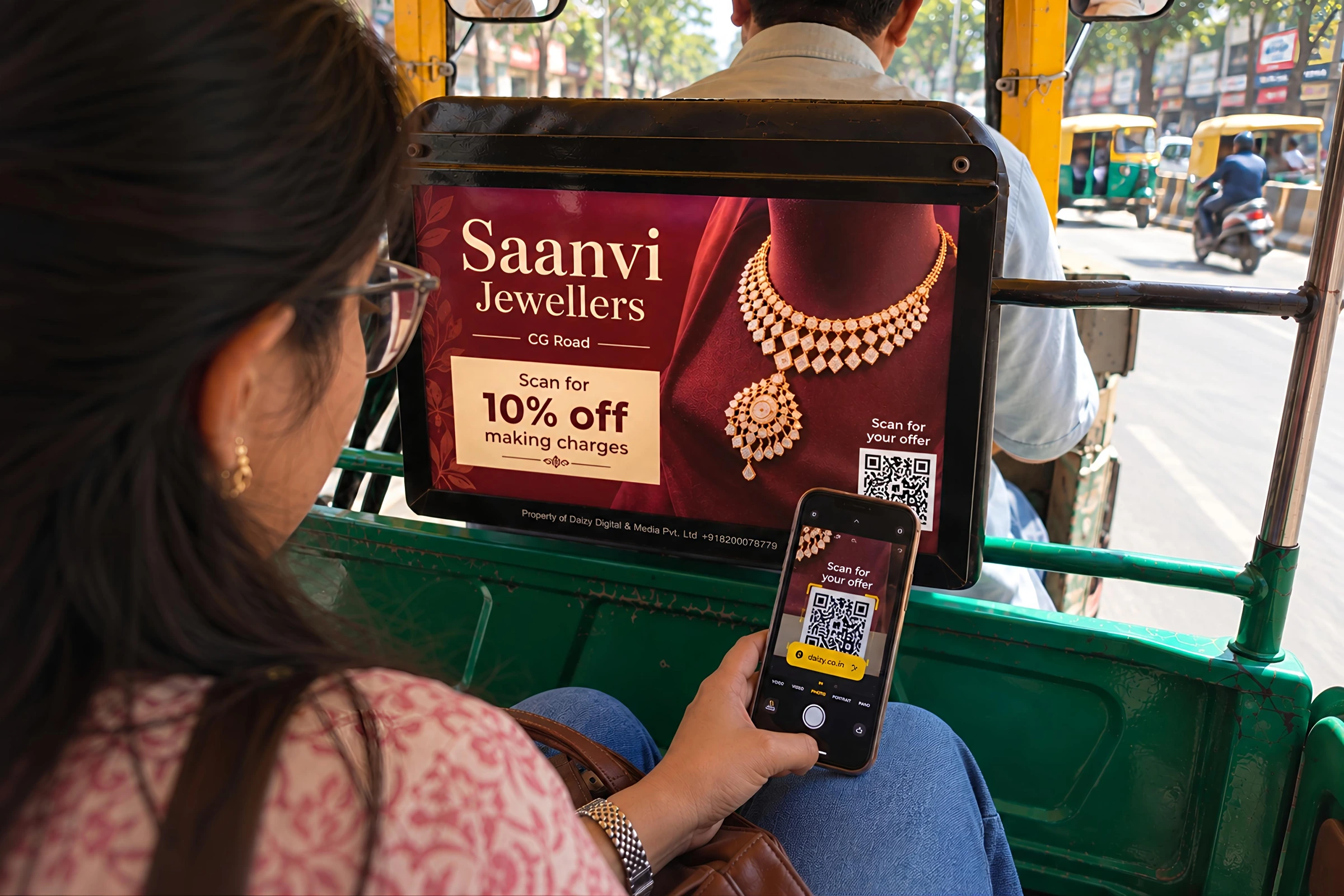 A passenger in an auto-rickshaw looking at a lit advertising board fixed to the back of the driver's seat.